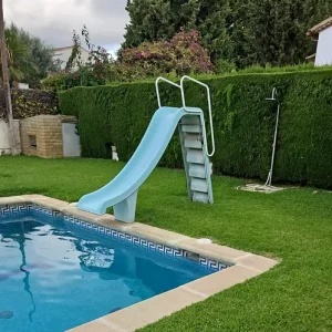 Tobogán para piscina instalado en jardín con césped junto a piscina privada